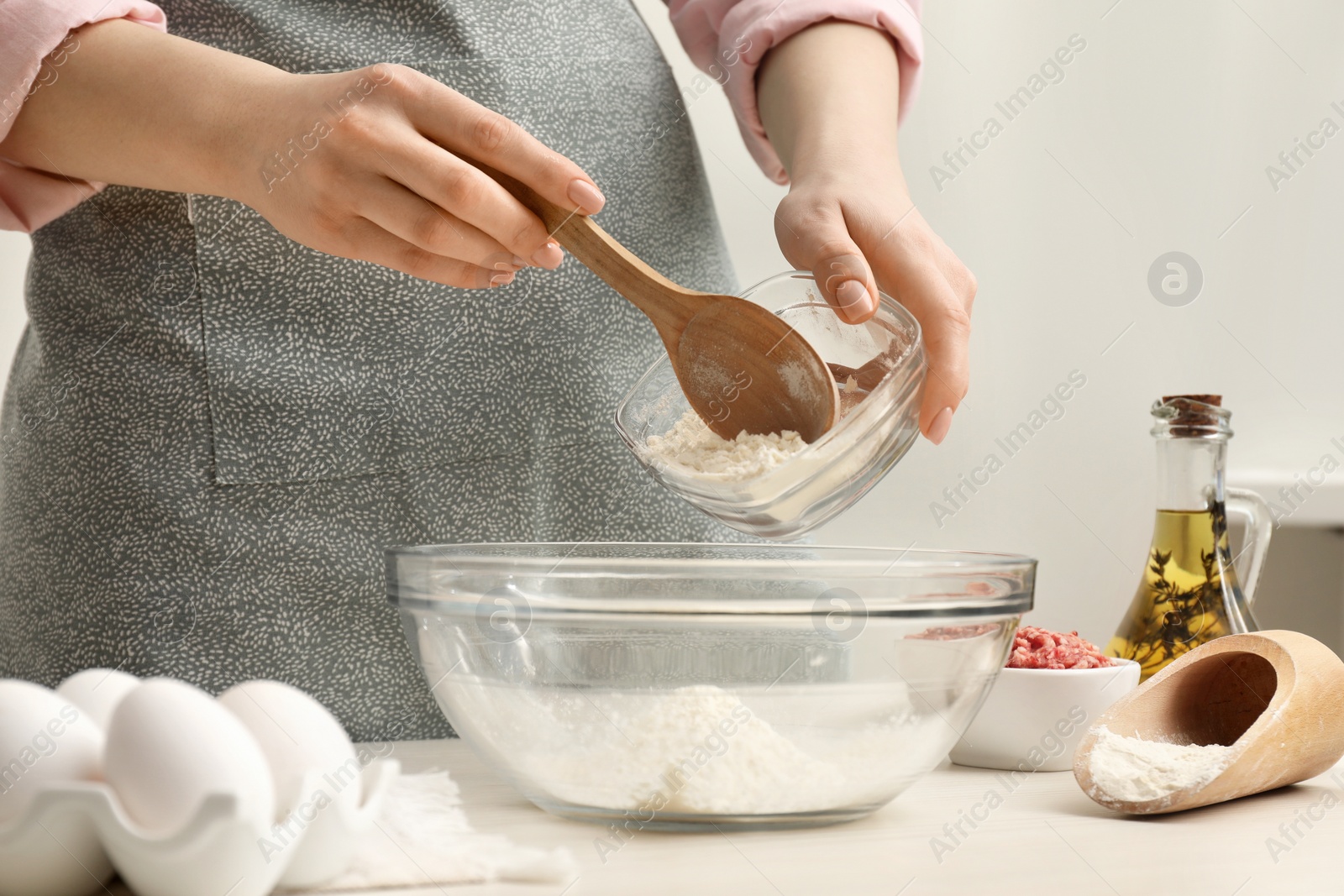 Photo of Woman putting flour into bowl at white wooden table, closeup