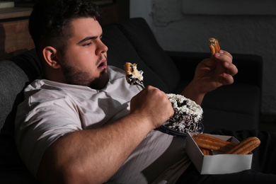 Photo of Depressed overweight man eating sweets in living room at night