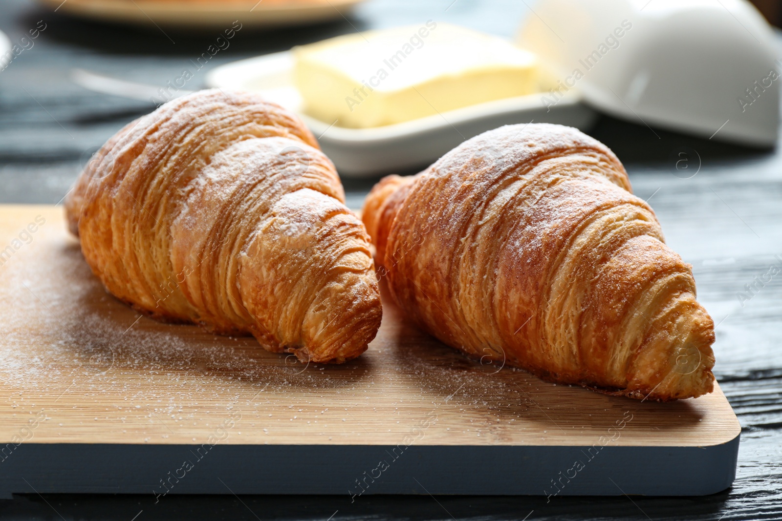 Photo of Wooden board with tasty croissants on table, closeup. French pastry