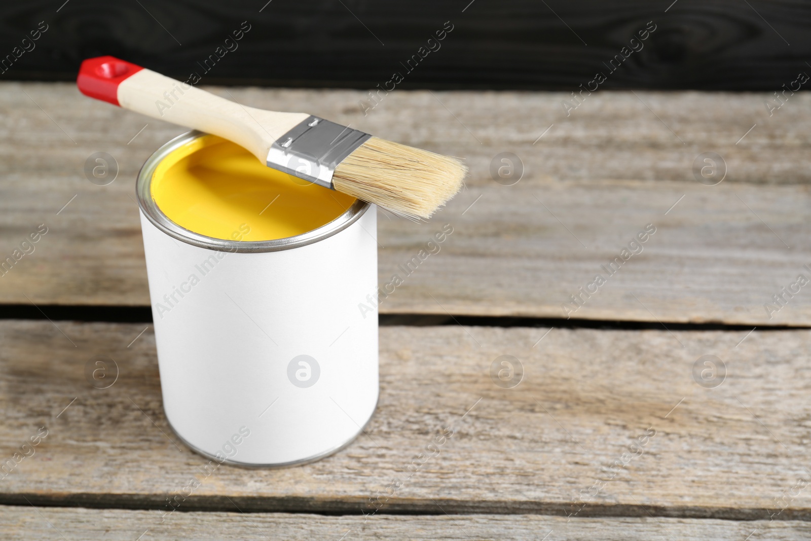 Photo of Can of yellow paint with brush on wooden table. Space for text