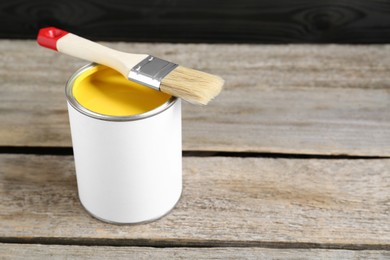 Photo of Can of yellow paint with brush on wooden table. Space for text