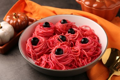 Photo of Red pasta with olives in bowl on grey textured table, closeup. Halloween food