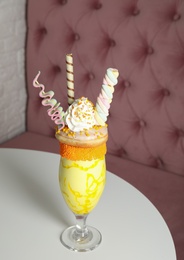Glass of tasty milk shake with sweets on table indoors