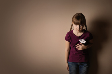 Sad little girl with sign HELP on beige background, space for text. Child in danger