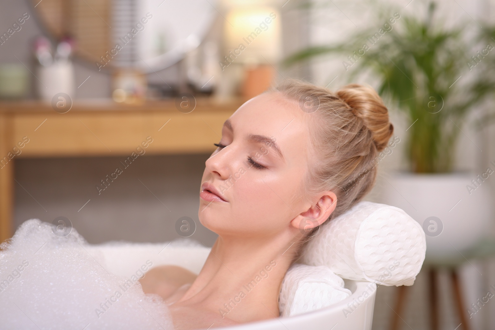 Photo of Young woman using pillow while enjoying bubble bath indoors