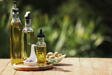 Different cooking oils and ingredients on wooden table against blurred green background, space for text