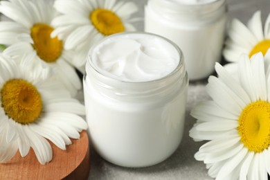 Photo of Jars of face cream and beautiful chamomiles on grey table