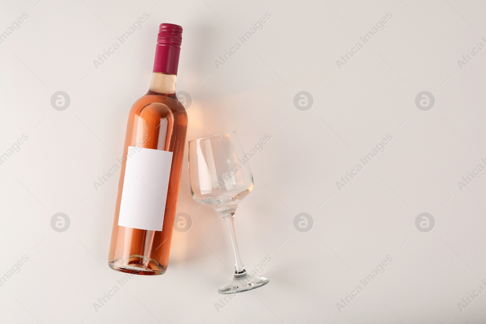 Photo of Bottle of tasty rose wine and glass on white background, flat lay. Space for text