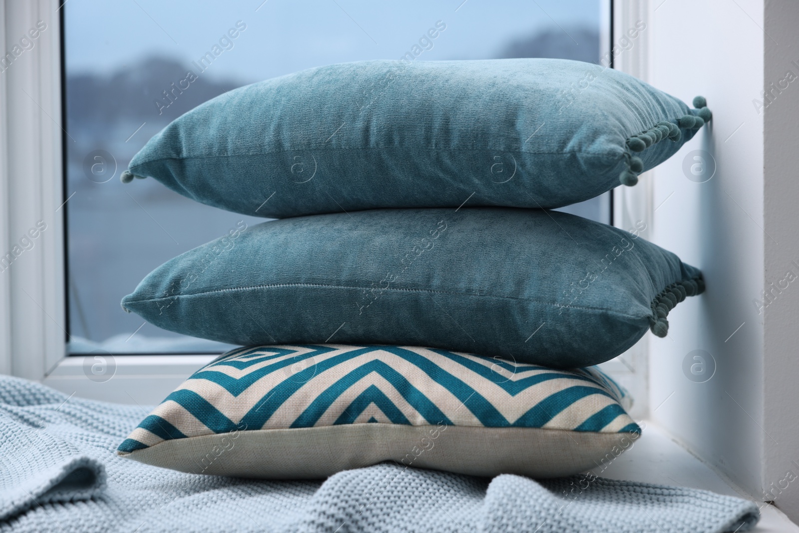 Photo of Stack of soft pillows and blanket on window sill indoors
