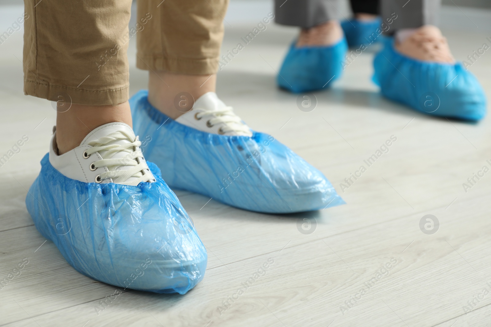 Photo of Women wearing blue shoe covers onto different footwear indoors, selective focus