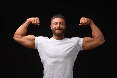 Photo of Young bodybuilder showing his muscular arms on black background