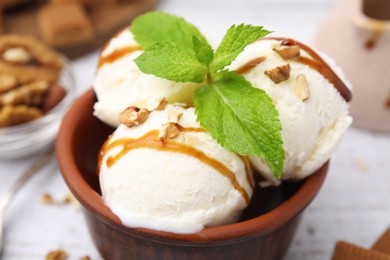 Photo of Bowl of tasty ice cream with caramel sauce, mint and nuts on table, closeup