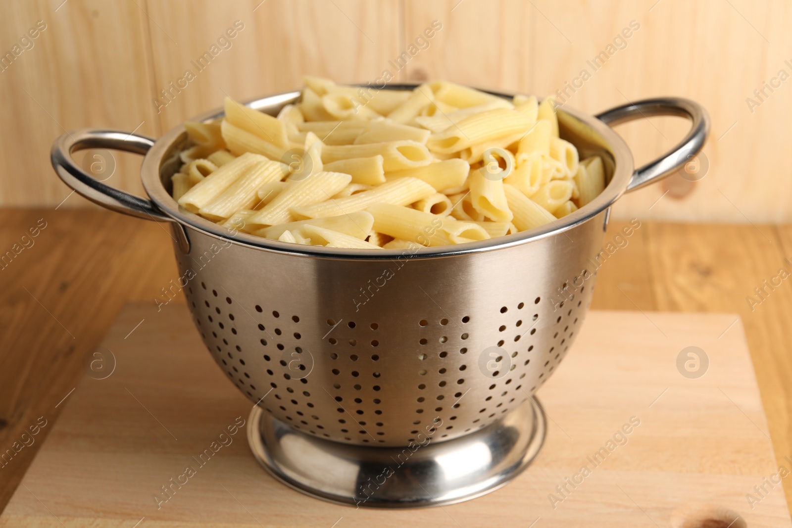 Photo of Cooked pasta in metal colander on wooden table, closeup