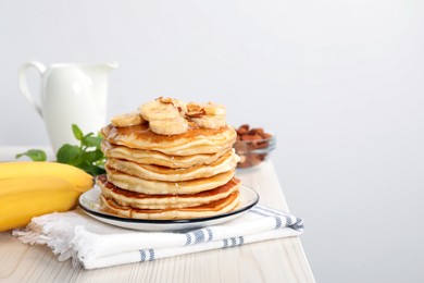 Photo of Tasty pancakes with sliced banana served on white wooden table. Space for text