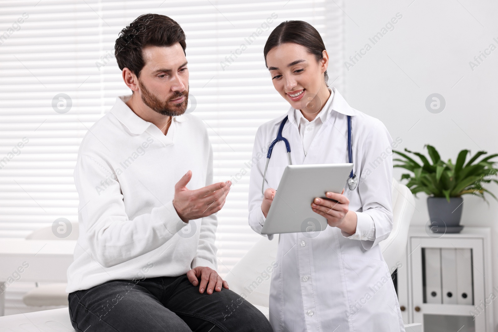 Photo of Doctor with tablet consulting patient during appointment in clinic