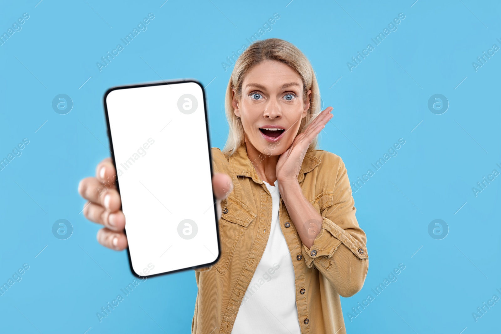 Photo of Surprised woman holding smartphone with blank screen on light blue background