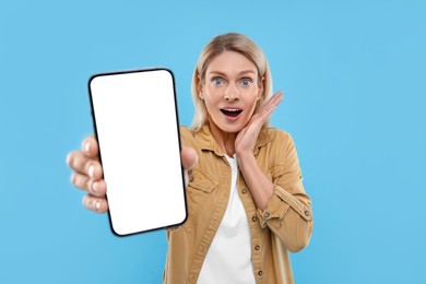 Photo of Surprised woman holding smartphone with blank screen on light blue background