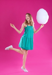 Happy young woman with cotton candy on pink background