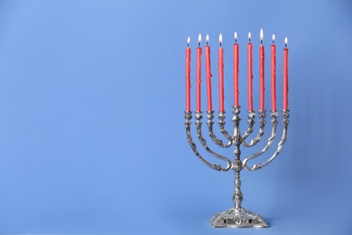 Photo of Silver menorah with burning candles on light blue background, space for text. Hanukkah celebration
