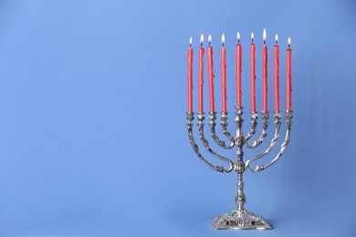 Silver menorah with burning candles on light blue background, space for text. Hanukkah celebration