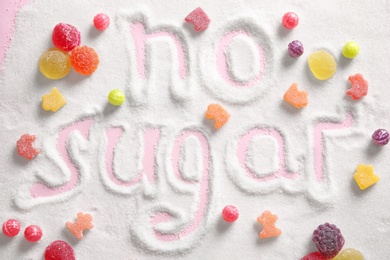 Photo of Composition with sweets and phrase NO SUGAR written on sugar sand