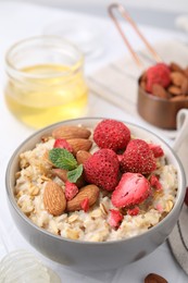 Photo of Delicious oatmeal with freeze dried strawberries, almonds and mint on table