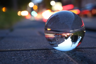 Beautiful city street, overturned reflection. Crystal ball on asphalt road outdoors, closeup. Space for text
