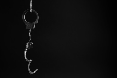 Photo of Classic chain handcuffs hanging on black background, space for text