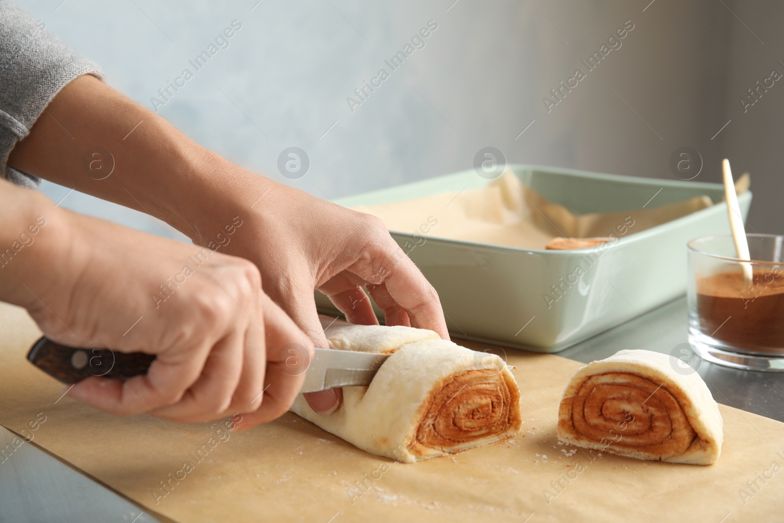 Photo of Woman cutting dough for cinnamon rolls on parchment at table, closeup