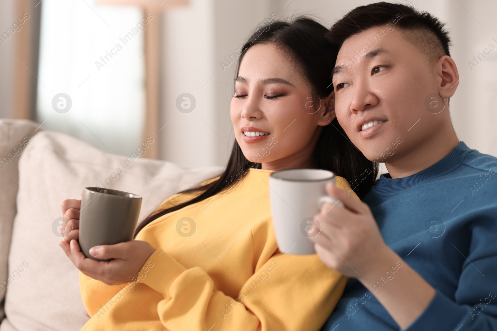 Photo of Happy couple with cups of drink on sofa at home