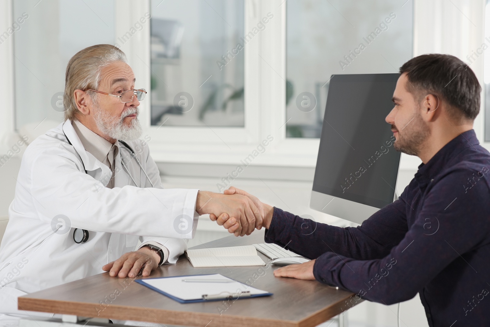 Photo of Senior doctor shaking hands with patient at wooden table in clinic