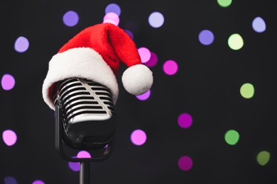 Photo of Retro microphone with Santa hat against blurred lights, space for text. Christmas music