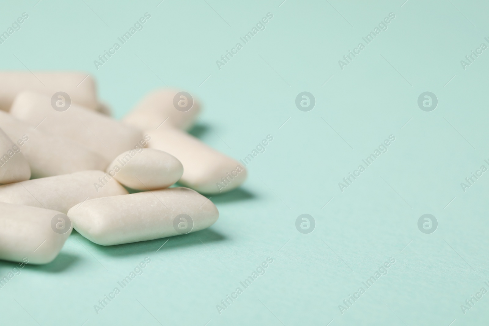 Photo of Many chewing gum pieces on turquoise background, closeup. Space for text
