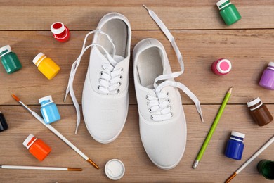 Photo of White sneakers and painting supplies on wooden table, flat lay. Customized shoes