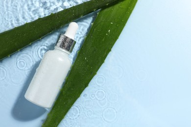 Photo of Bottle of cosmetic product and aloe leaves in water on light blue background, flat lay. Space for text