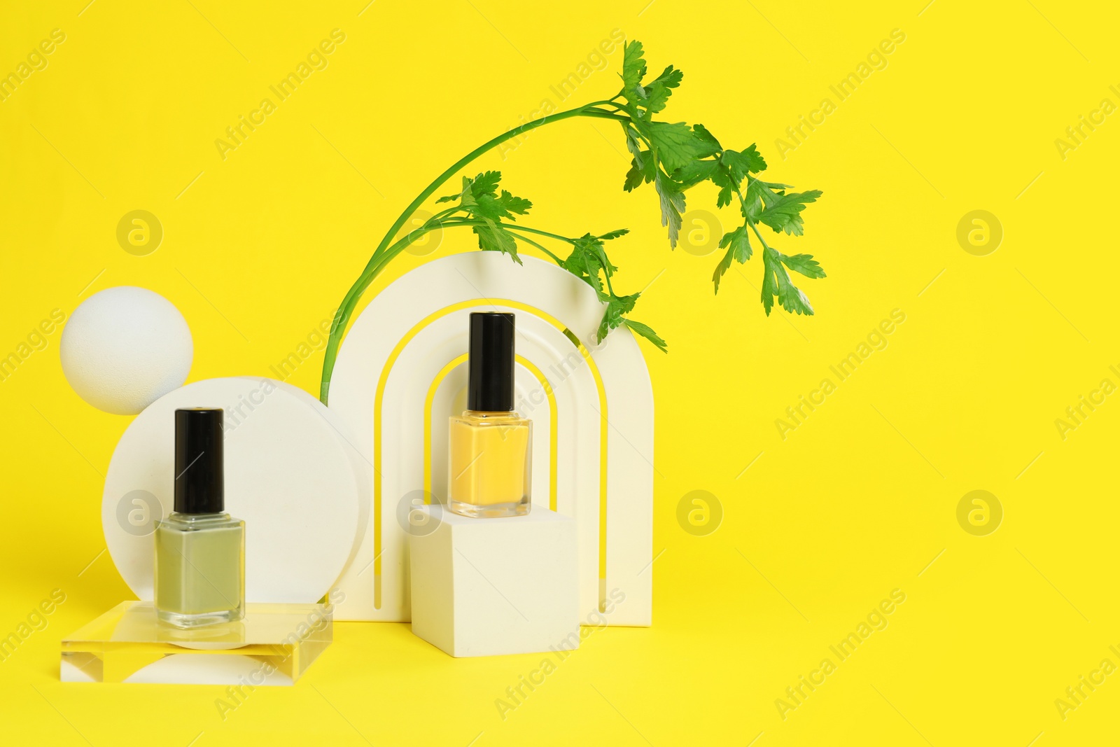 Photo of Stylish presentation of beautiful nail polishes in bottles on yellow background. Space for text