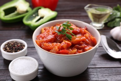 Photo of Bowl of delicious lecho with parsley on black wooden table, closeup