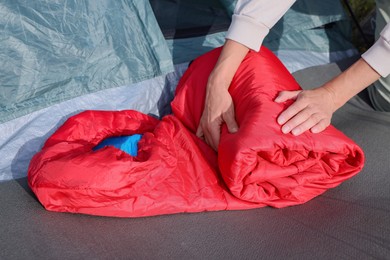 Woman folding red sleeping bag near camping tent outdoors, closeup
