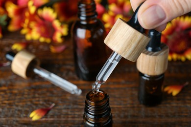 Photo of Woman pouring essential oil from pipette into bottle on wooden table, closeup