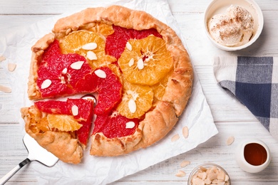 Photo of Tasty galette with citrus fruits served on white wooden table, flat lay