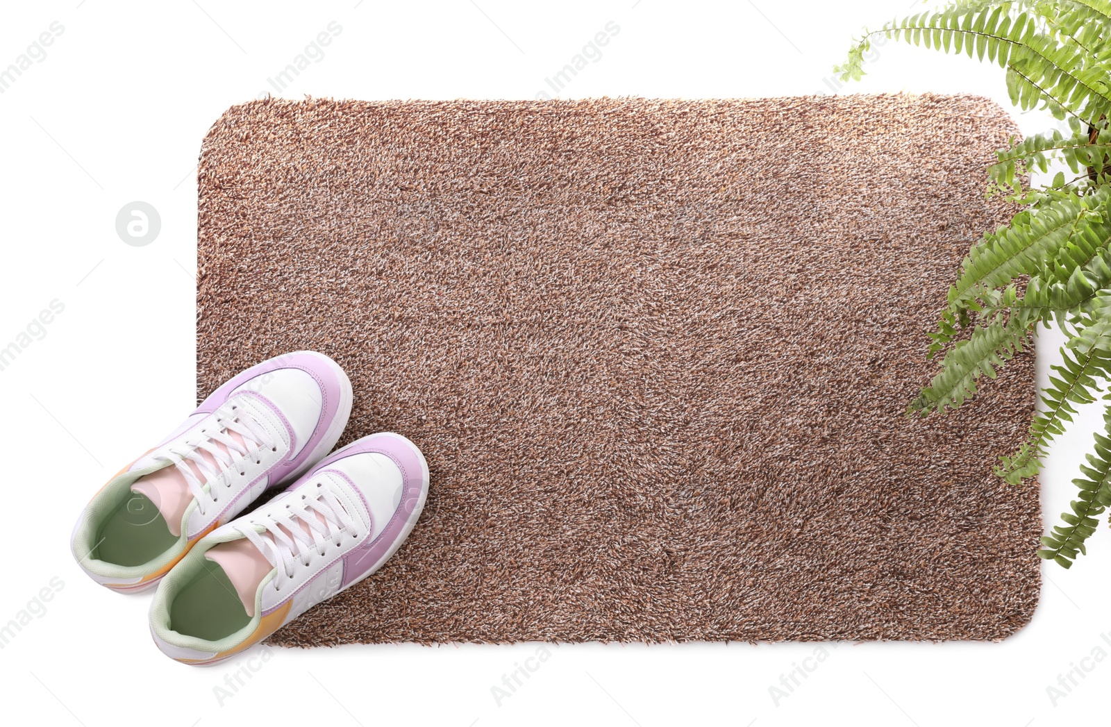 Photo of Stylish door mat with shoes and plant on white background, top view