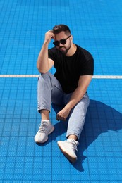 Handsome man in sunglasses on blue floor covering outdoors