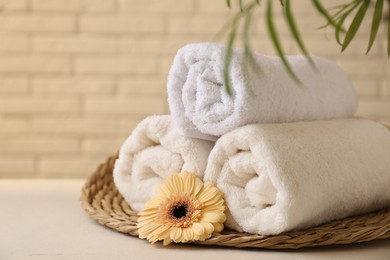 Photo of Rolled terry towels, flower and green leaves on white table near brick wall indoors, closeup. Space for text