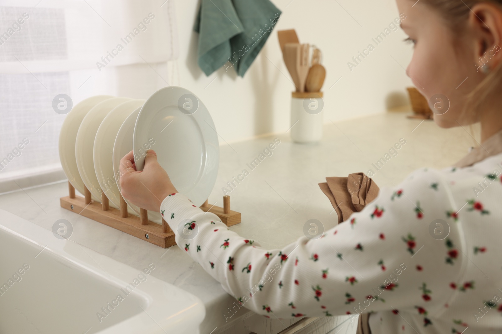 Photo of Girl putting clean plate on drying rack in kitchen, closeup