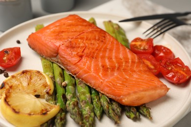 Photo of Tasty grilled salmon with asparagus, tomatoes and lemon on plate, closeup