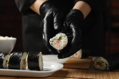 Photo of Chef in gloves putting sushi roll onto dish at table, closeup