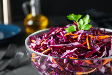 Photo of Bowl with fresh red cabbage salad on grey kitchen table, closeup