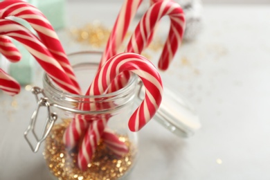 Photo of Christmas candy canes in glass jar on light background, closeup