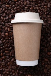 Photo of Coffee to go. Paper cup on roasted beans, top view