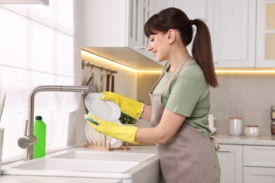 Photo of Happy young housewife washing dishes in kitchen sink. Cleaning chores